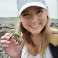 White woman with blonde hair, white hat, holding a small crab